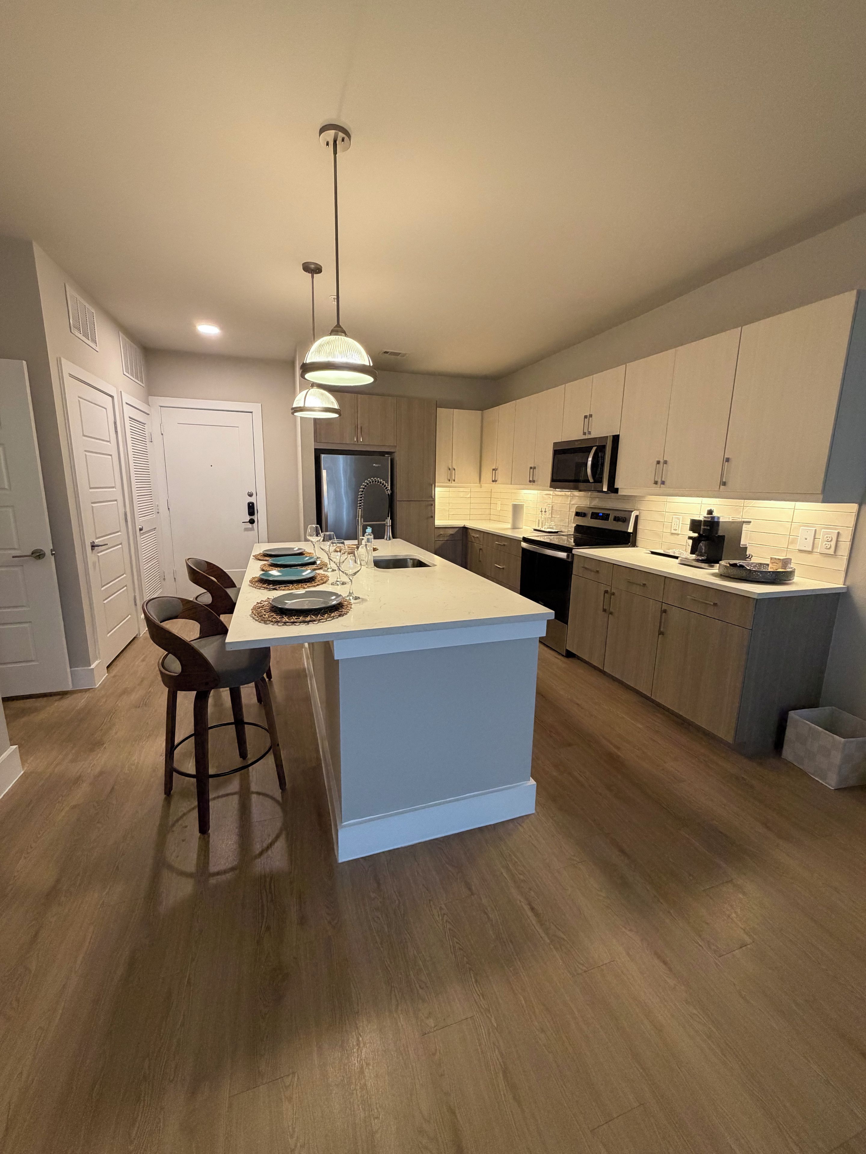 A modern kitchen with a central island, bar stools, a microwave, and a dishwasher.