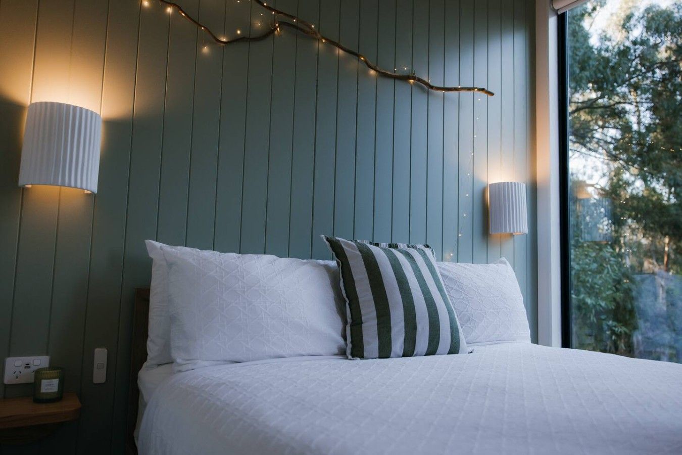 A bedroom with a bed, two bedside lamps, and a string of lights on the wall.