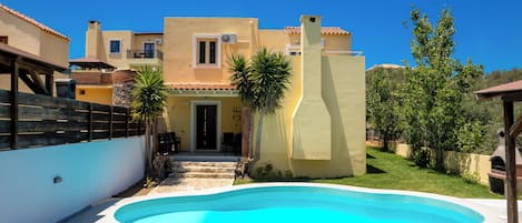 A swimming pool with lounge chairs, a building with a balcony, and a clear blue sky.