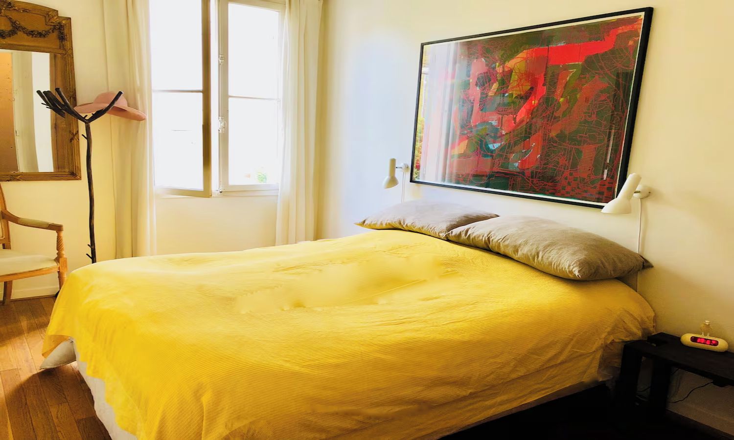 A bedroom with a bed, a chair, a window, and a painting on the wall.