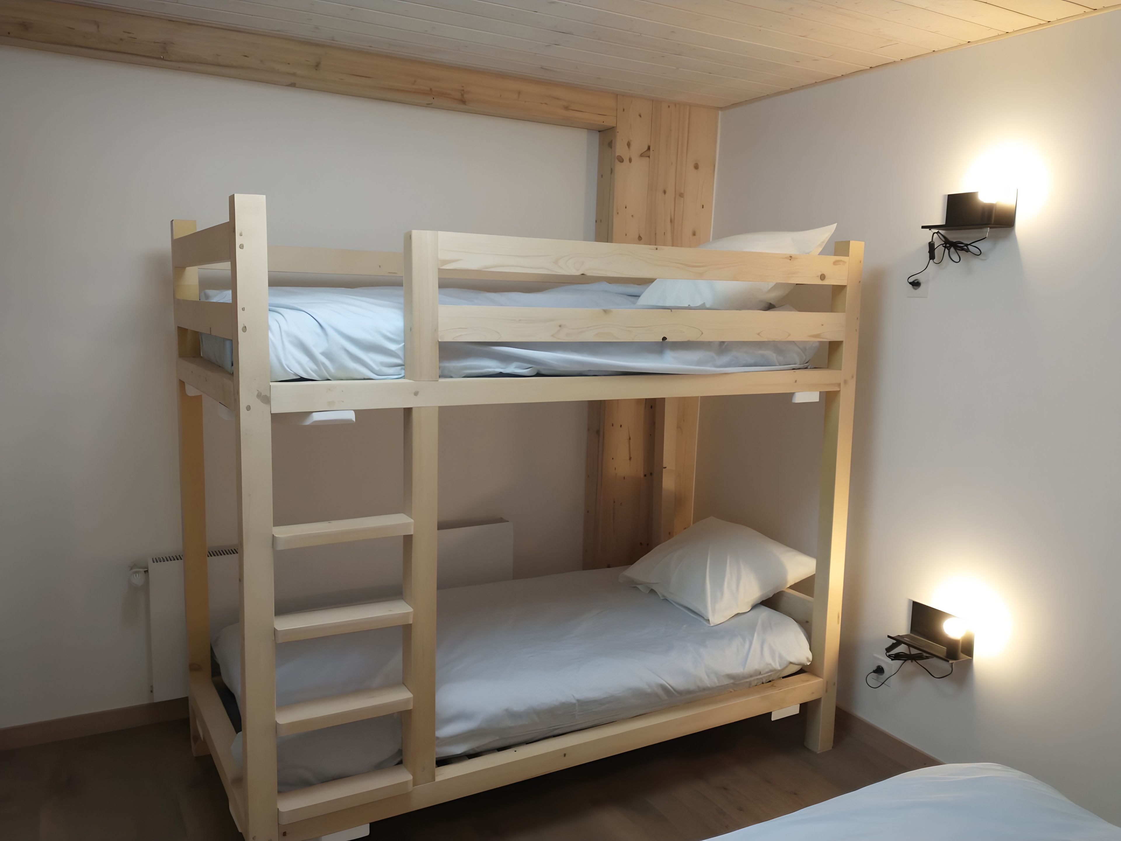 Un lit superposé avec une structure en bois, une literie blanche et un luminaire fixé au mur.