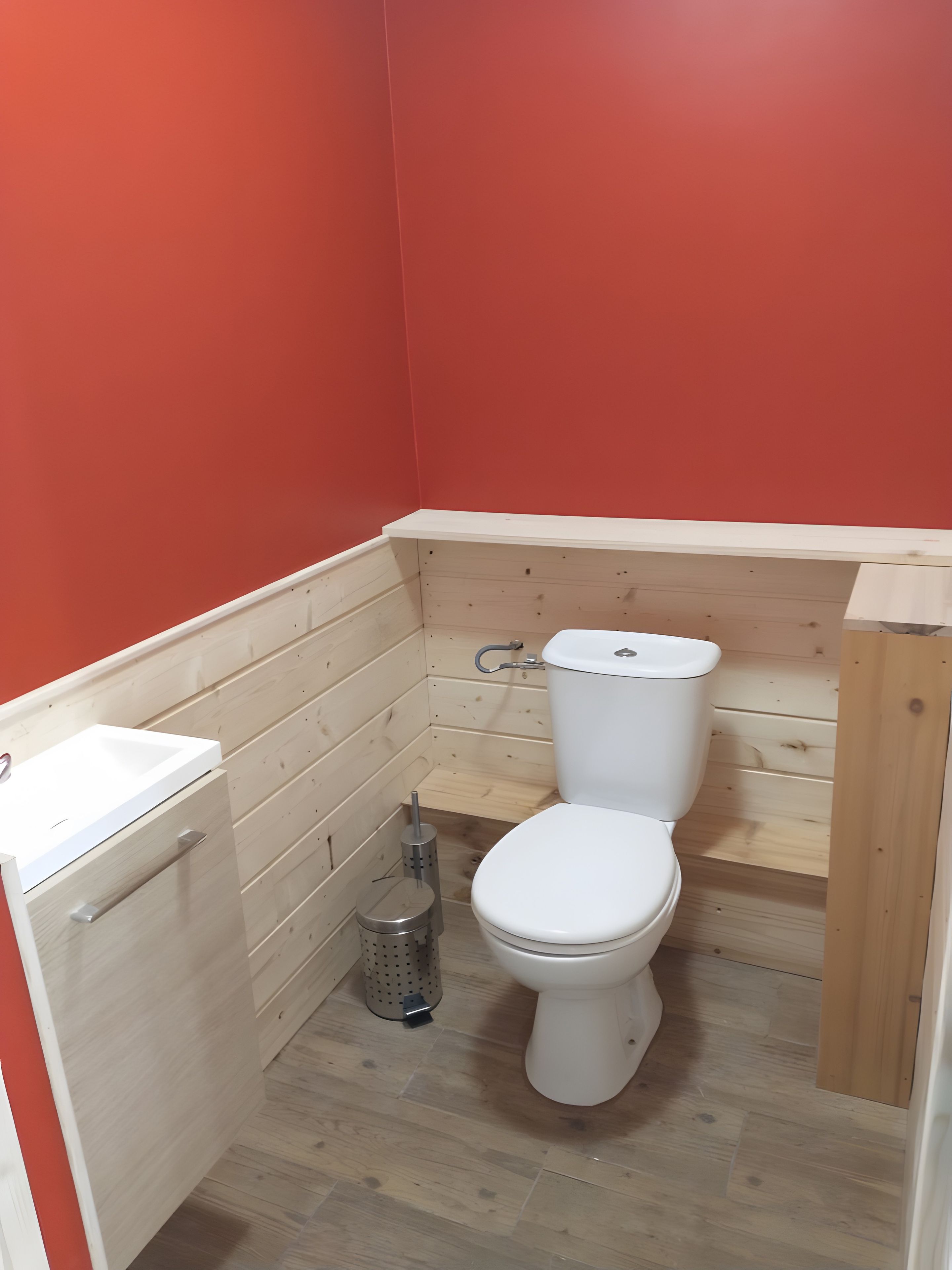 Une petite salle de bain avec des toilettes blanches, un petit lavabo et une poubelle.