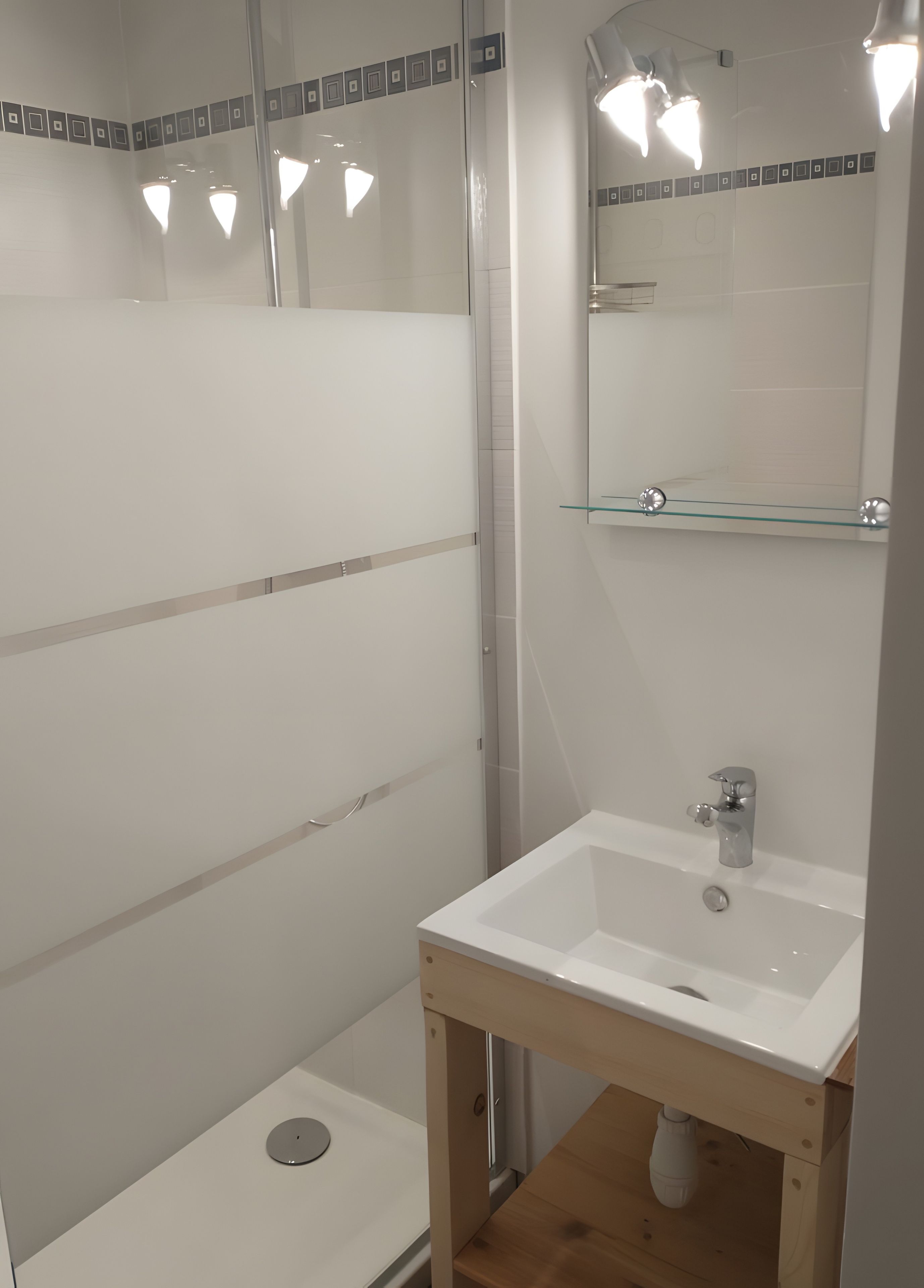 Une salle de bain avec une douche à parois de verre, un lavabo blanc doté d’un meuble en bois et un miroir avec éclairage intégré.