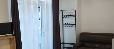 A living room with a sofa, a coffee table, a TV on a stand, a coat rack, and a suitcase.