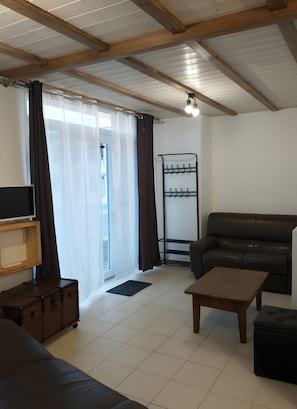 A living room with a sofa, a coffee table, a TV on a stand, a coat rack, and a suitcase.