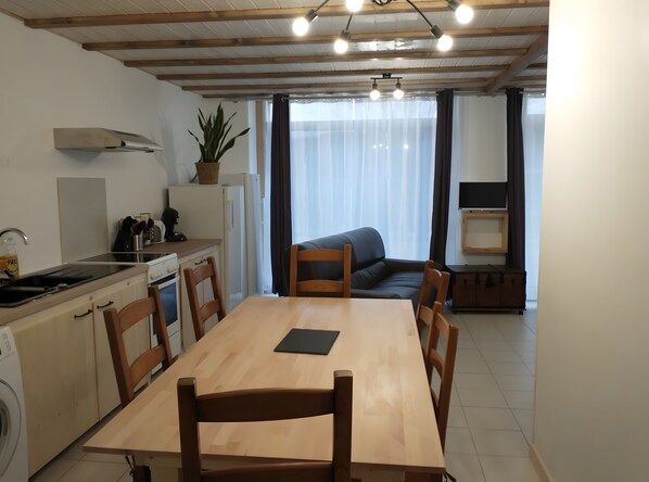 A compact kitchen with a dining area, wooden furniture, and a large window with curtains.
