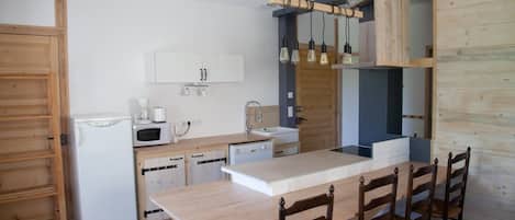 Eine kleine Küche mit Holztisch, vier Stühlen, einer Mikrowelle, einem Spülbecken und hängenden Pendelleuchten.