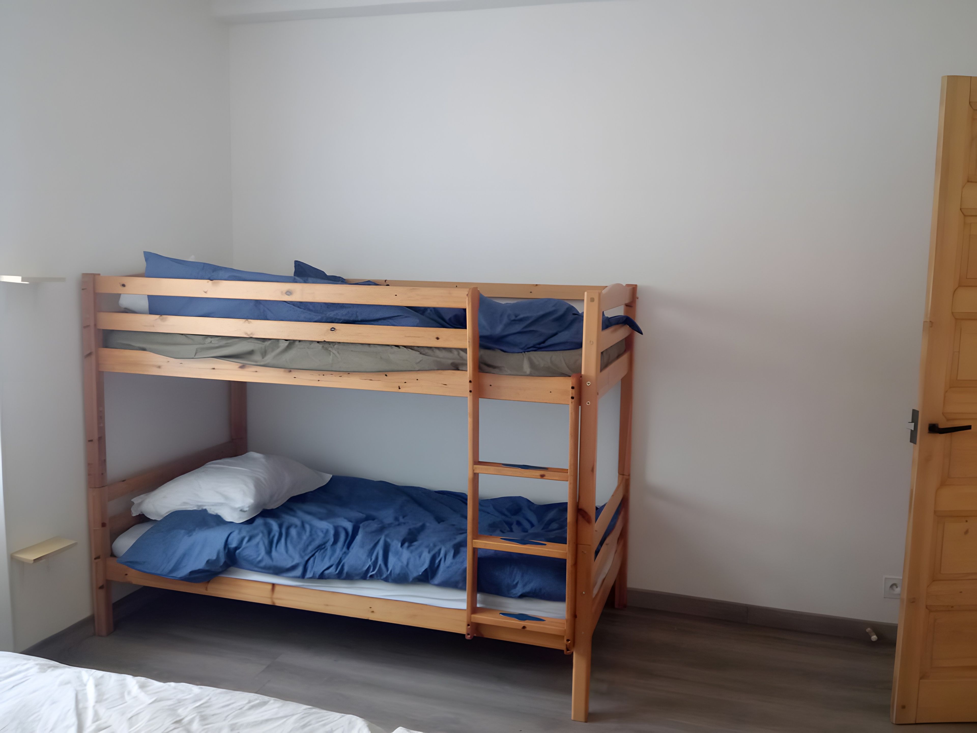 A bunk bed with blue bedding in a room with a wooden door and a light-colored floor.