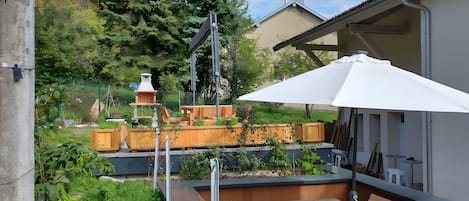 A patio with a wooden table and bench, a white umbrella, and a brick barbecue grill.