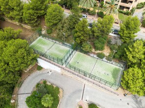 Eine Vogelperspektive zeigt eine Wohngegend mit zwei eingezäunten Tennisplätzen, umgeben von Bäumen und einer gewundenen Straße.