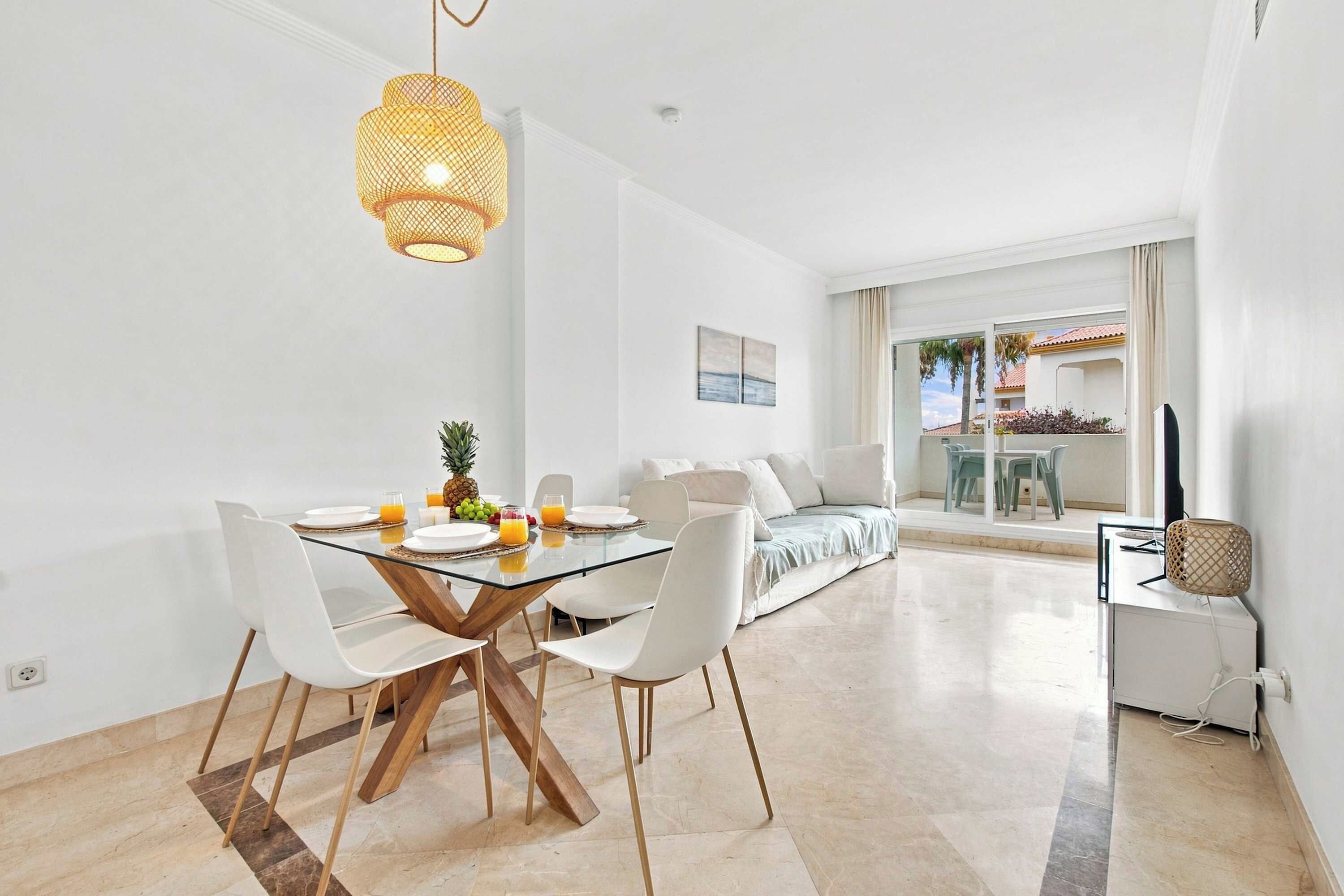 A modern dining area with a glass table, white chairs, and a hanging light fixture.