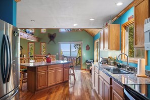 A kitchen with wooden cabinets, a granite countertop, a stainless steel refrigerator, and a view of the outdoors. - MACKINAW STRAITS & BRIDGE VIEW 4 BEDROOM PRIVATE CABIN & BEACH (Cheboygan)