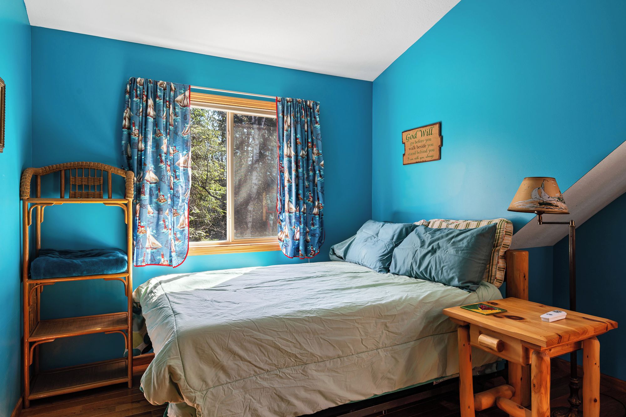 A room with a bed, a wooden chair, a small table, and a window with curtains.
