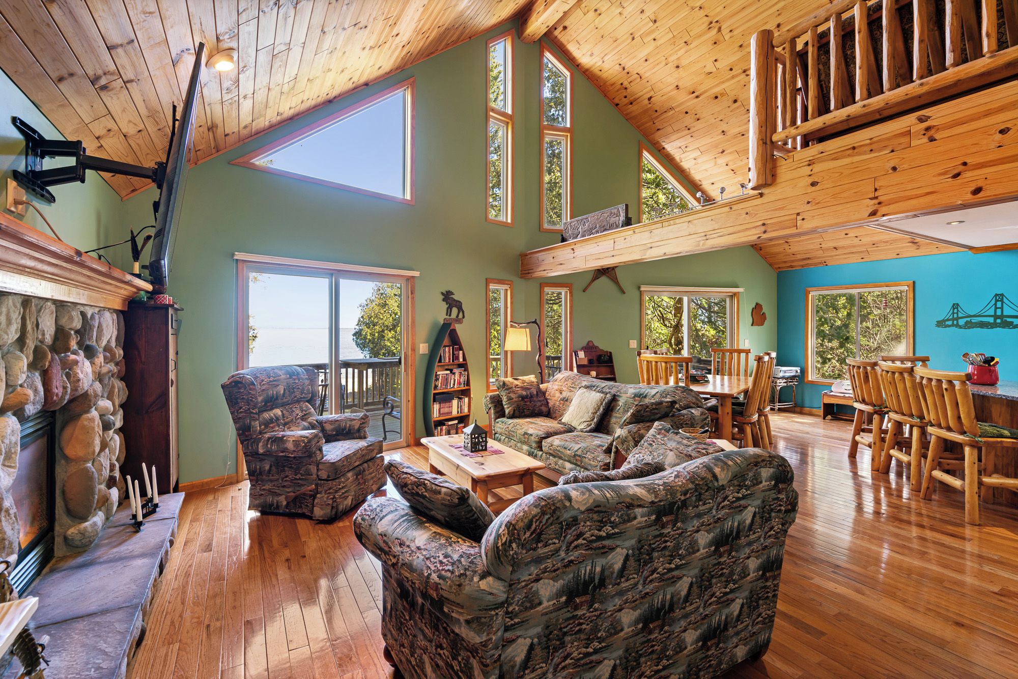 A spacious living area with a high ceiling, large windows, and a stone fireplace.