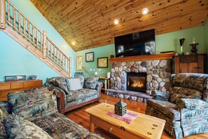 A cozy living room with a stone fireplace, a wooden staircase, and a flat-screen TV mounted above it. - MACKINAW STRAITS & BRIDGE VIEW 4 BEDROOM PRIVATE CABIN & BEACH (Cheboygan)