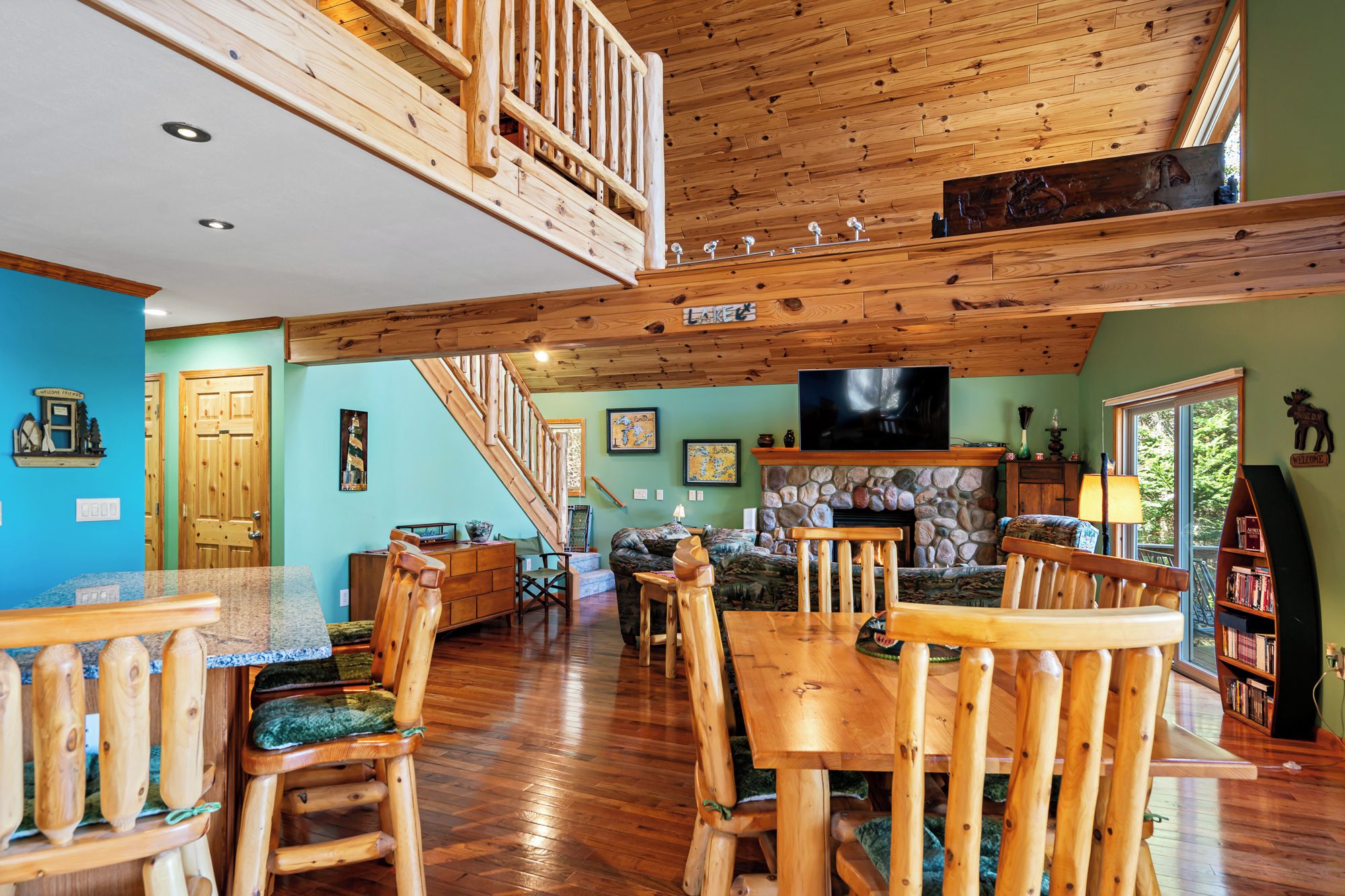 A spacious living area with a high ceiling, wooden furniture, a stone fireplace, and a television.