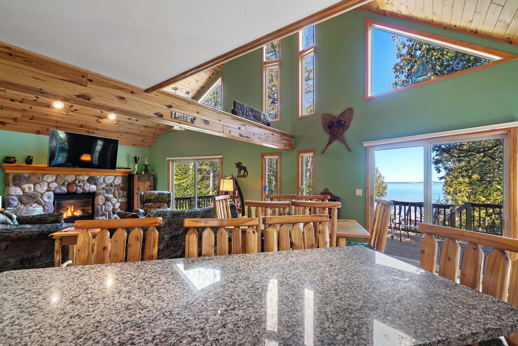 A spacious room with a stone fireplace, wooden ceiling beams, and a large window overlooking a body of water.