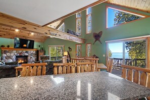 A spacious room with a stone fireplace, wooden ceiling beams, and a large window overlooking a body of water. - MACKINAW STRAITS & BRIDGE VIEW 4 BEDROOM PRIVATE CABIN & BEACH (Cheboygan)