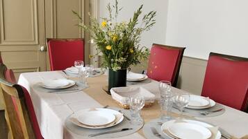 Mesa de jantar posta para quatro com toalhas brancas, cadeiras vermelhas e um vaso de flores.