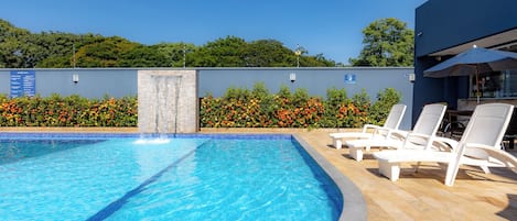 Piscina con borde de azulejos, rodeada por una terraza de madera y un área de descanso con sillones.