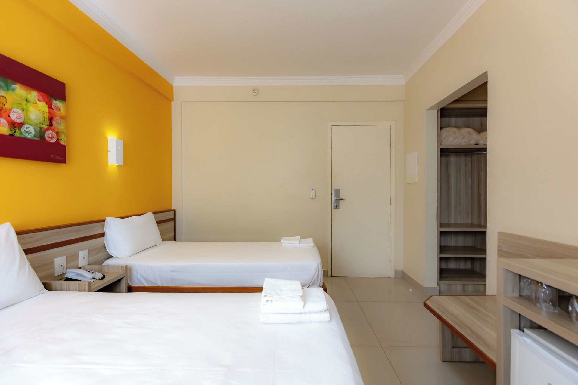 Una camera d'albergo con due letti, un armadio e un quadro appeso al muro.