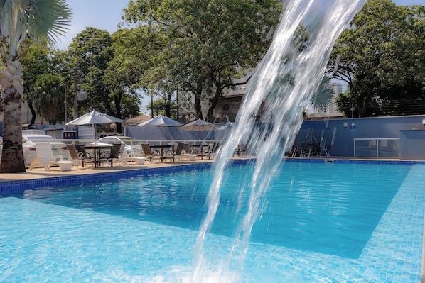 A swimming pool with a waterfall feature, surrounded by lounge chairs and umbrellas.