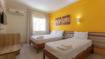 A hotel room with two beds, a desk, a TV, and a window with curtains.