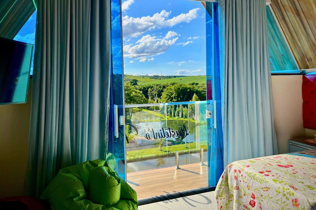 Een kamer met een grote schuifglazen deur die uitkomt op een balkon met een prachtig uitzicht op een groen landschap en een heldere lucht.