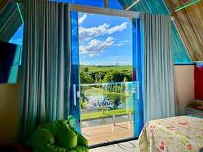 Una habitación con un amplio ventanal corredero que da a un balcón con vistas panorámicas a un paisaje verde y un cielo despejado.