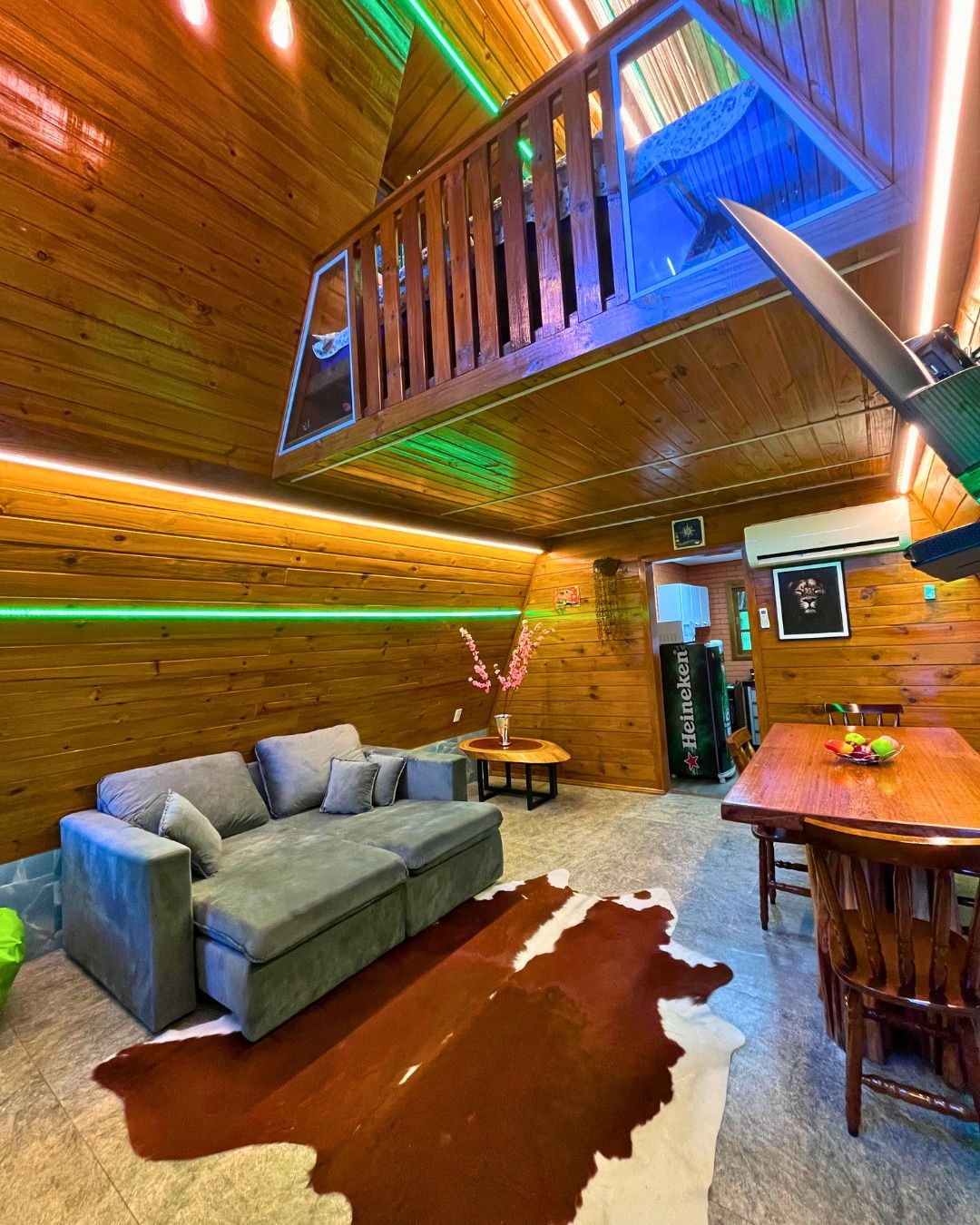 A wooden interior with a sofa, a dining table, and a ceiling with wooden beams and green lighting.