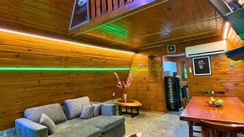 Un interior de madera con un sofá, una mesa de comedor y un techo con vigas de madera e iluminación verde.