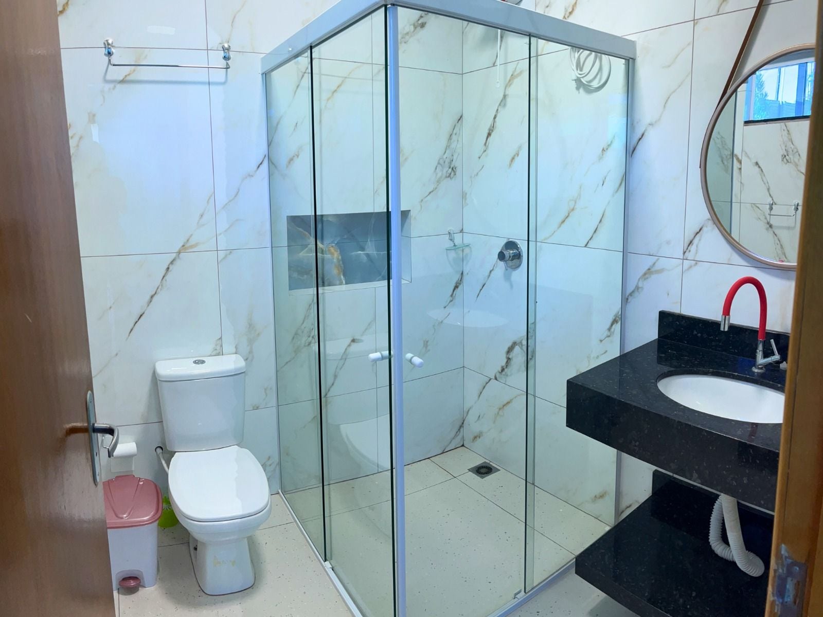 A bathroom with a glass-enclosed shower, a white toilet, and a black sink with a red faucet.