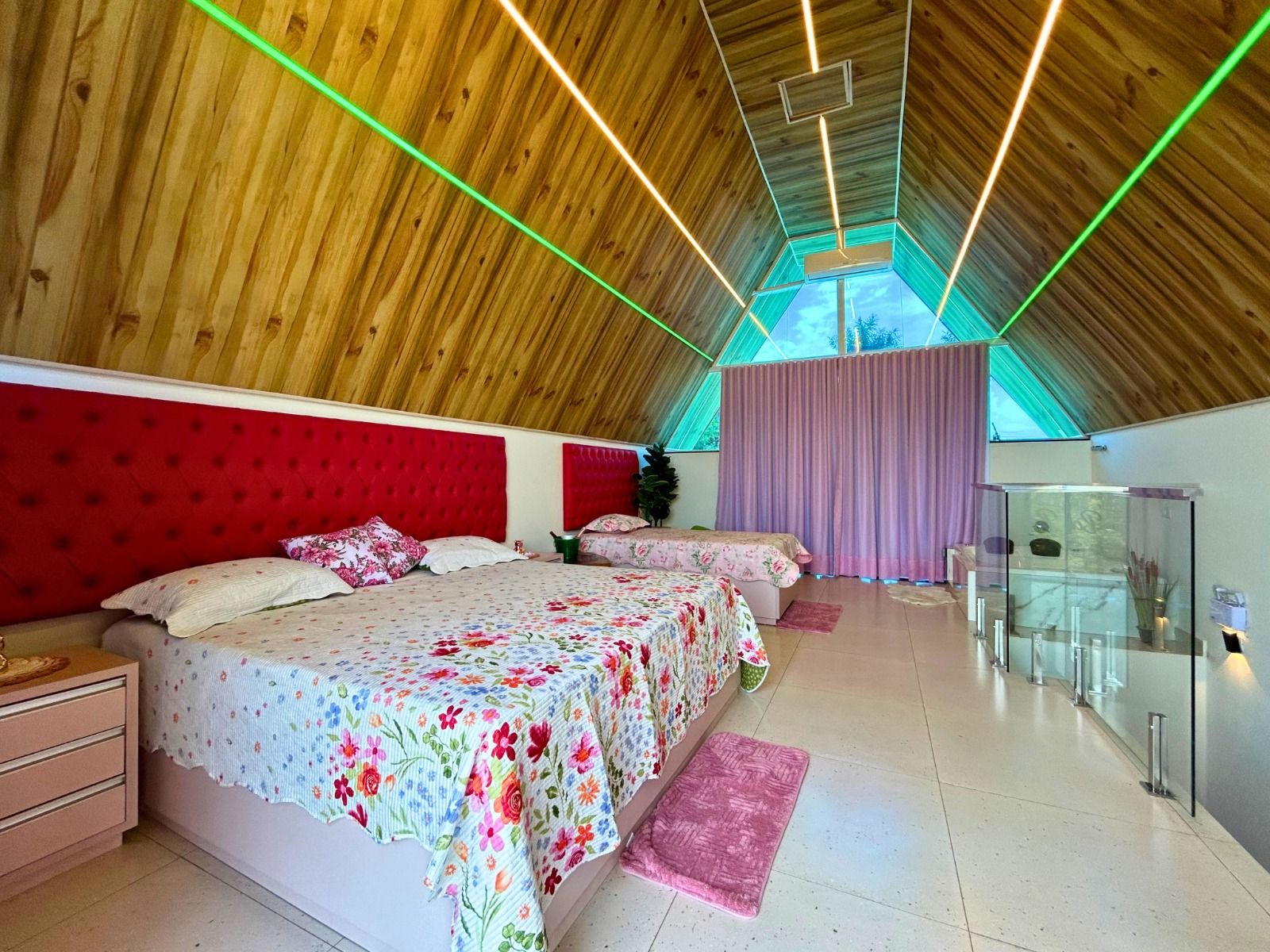 A bedroom with a sloped ceiling, a bed with floral bedding, a red headboard, and a glass cabinet.