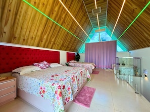 A bedroom with a sloped ceiling, a bed with floral bedding, a red headboard, and a glass cabinet.