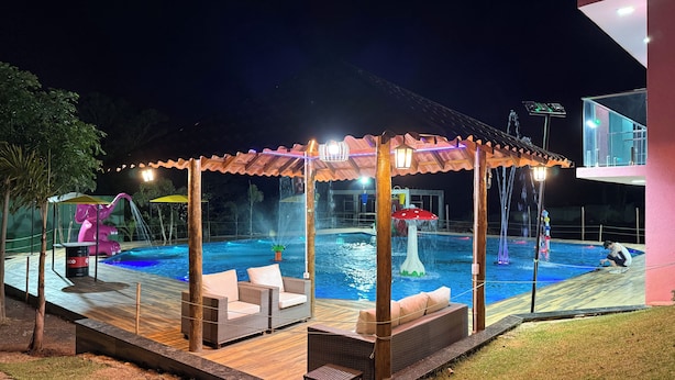 Un área de piscina al aire libre con una zona de estar techada, una fuente de agua y un edificio al fondo.