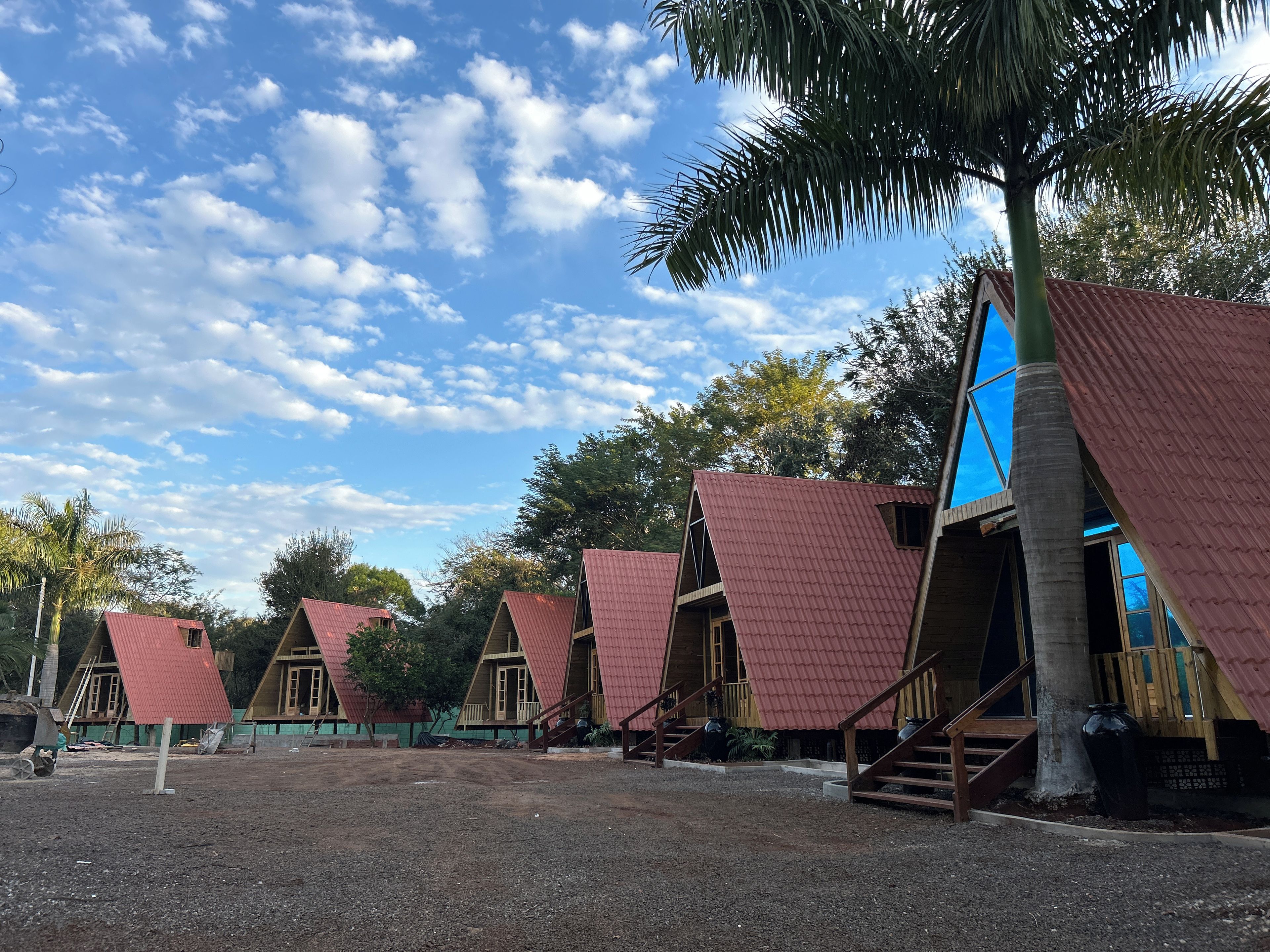 A row of triangular-roofed cabins with wooden staircases leading to the entrance, surrounded by trees and a clear sky.