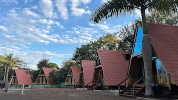 A row of triangular-roofed cabins with wooden staircases leading to the entrance, surrounded by trees and a clear sky.