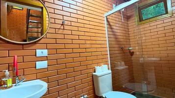 Un baño con pared de ladrillo, lavamanos, inodoro, espejo y ducha.