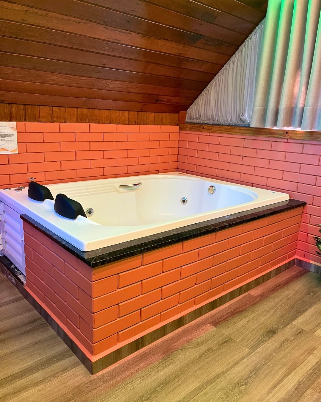 Un jacuzzi con un fondo de pared de ladrillo, techo de madera y piso de madera.