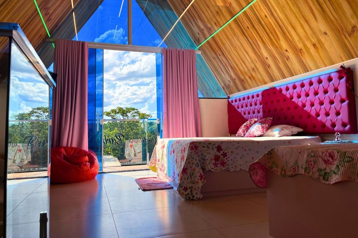 Een slaapkamer met een groot bed, een rode relaxstoel en uitzicht op de lucht door een glazen deur.