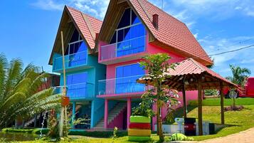 Un edificio de varios pisos con techo rojo, paredes azules y rosadas, y grandes ventanales.