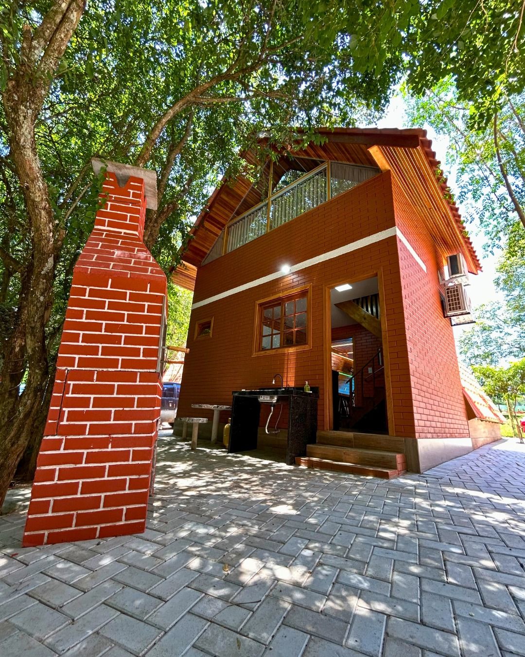 A two-story building with a brick chimney, a balcony, and a paved entrance area.