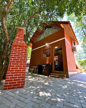 A two-story building with a brick chimney, a balcony, and a paved entrance area.