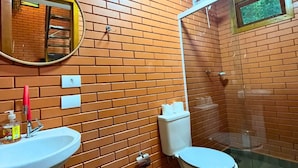 Un baño con pared de ladrillo, lavamanos, inodoro, espejo y ducha.