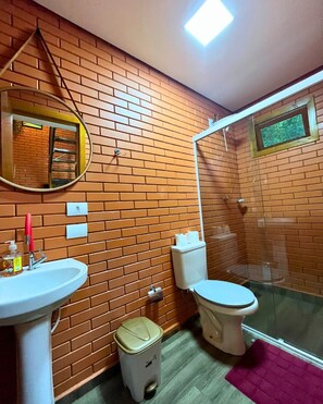 Een badkamer met een bakstenen muur, een wastafel, toilet, spiegel en douche.