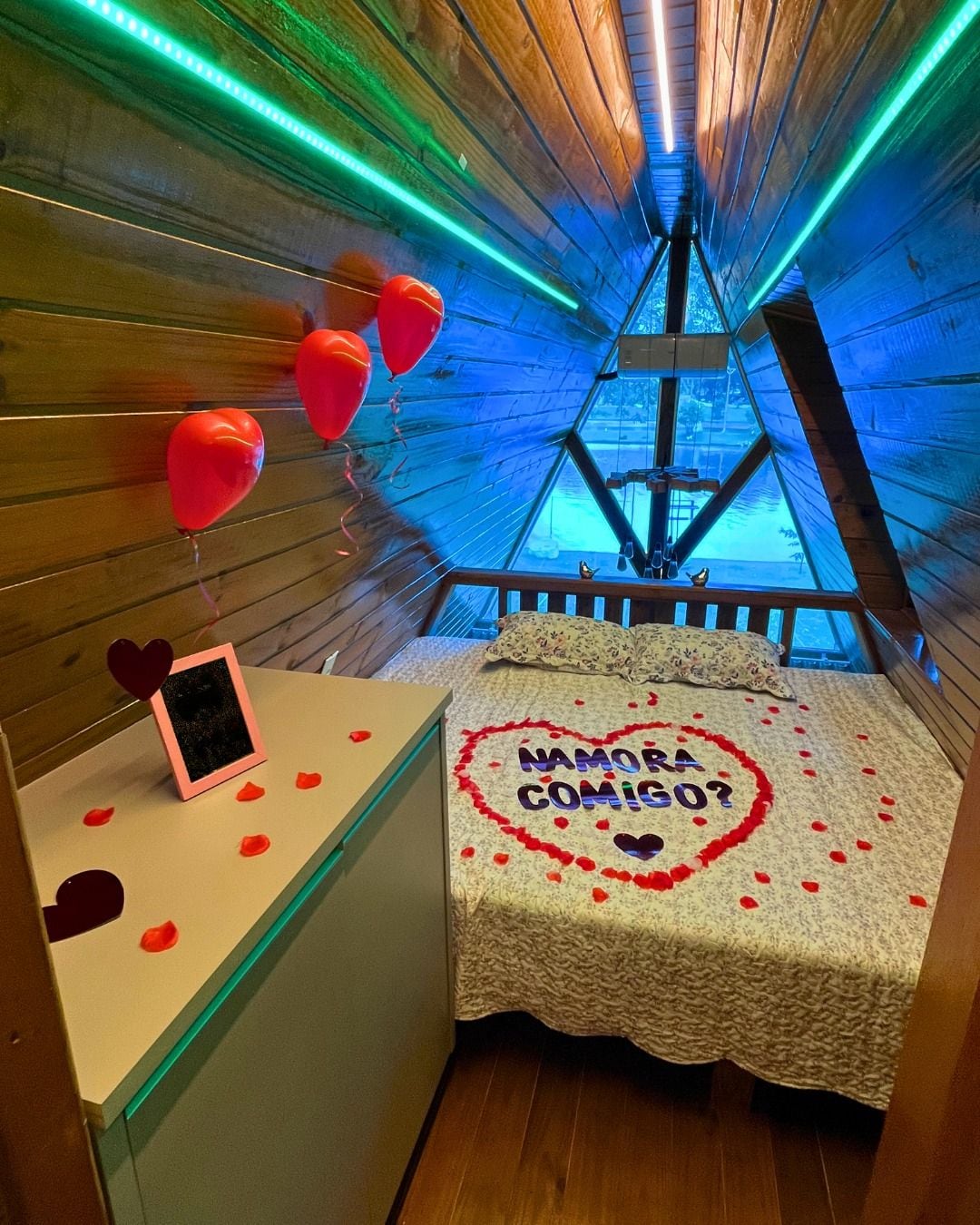 A room with a bed, a small table, and a wall decorated with balloons and a heart-shaped arrangement of rose petals.
