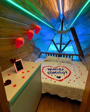 A room with a bed, a small table, and a wall decorated with balloons and a heart-shaped arrangement of rose petals.