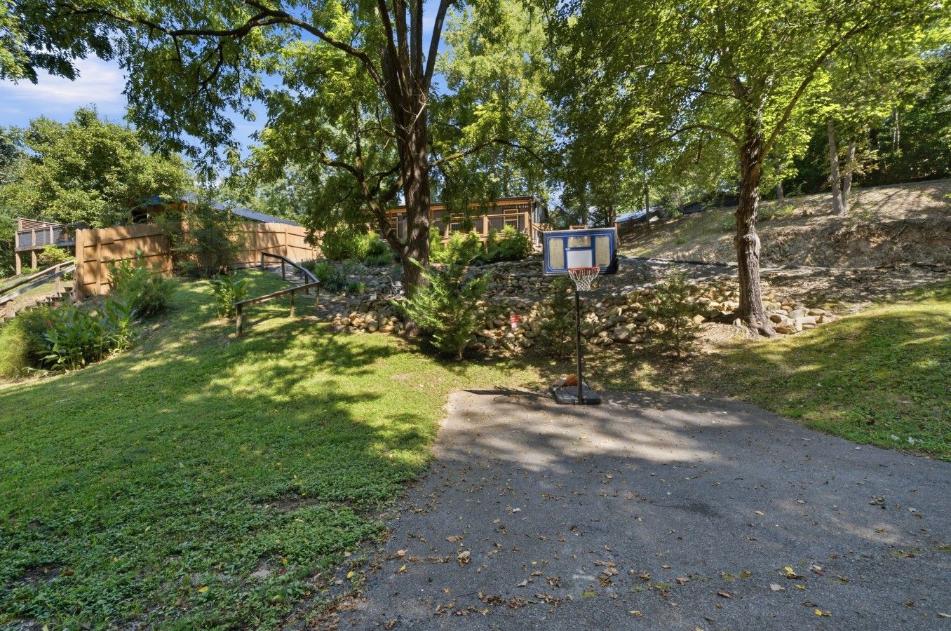 A residential area with a paved driveway, a basketball hoop, and a stone wall.