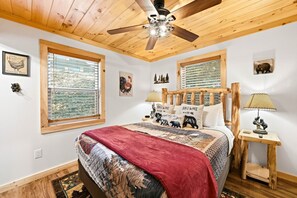 Ein Schlafzimmer mit einem Bett, Deckenventilator, zwei Fenstern, einem Holz-Kopfteil und einem Nachttisch mit Lampe.