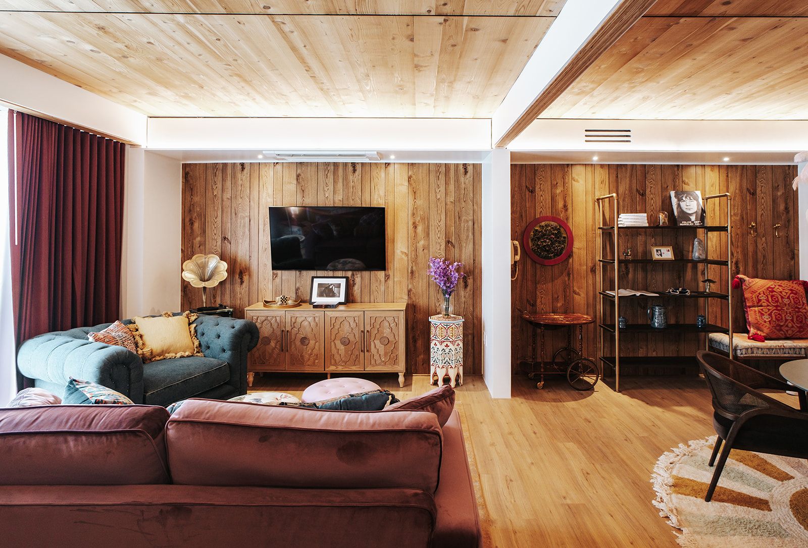 Una sala de estar con techo de madera, un televisor de pantalla plana en la pared, un sofá, una mesa de centro y una estantería.